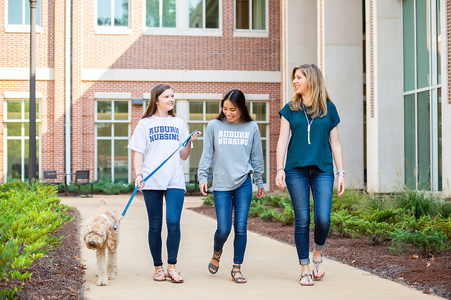 Three students walking a dog outside the Nursing building.